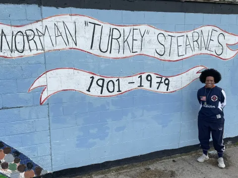 Picture of author Vaness Ivy Rose posing next to a wall mural dedicated to "Norman Turkey Stearnes"