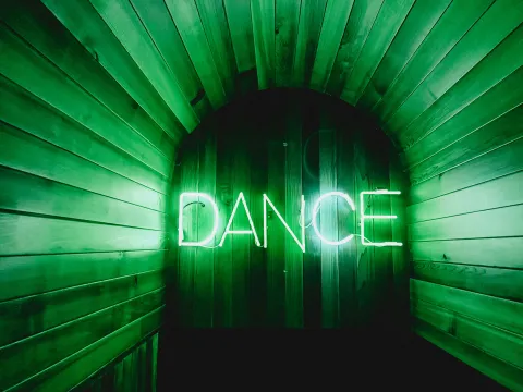 Wooden wall with bright neon green sign that says "Dance"