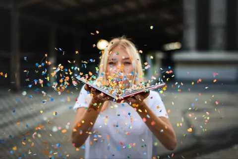 tween girl blowing confetti out of an open book