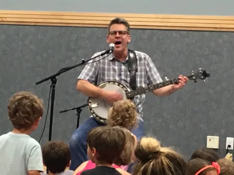 man playing banjo in front of kids