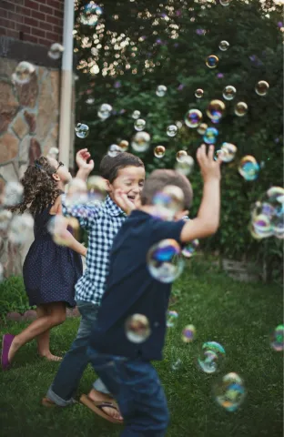 Children dance outside in a cloud of bubbles