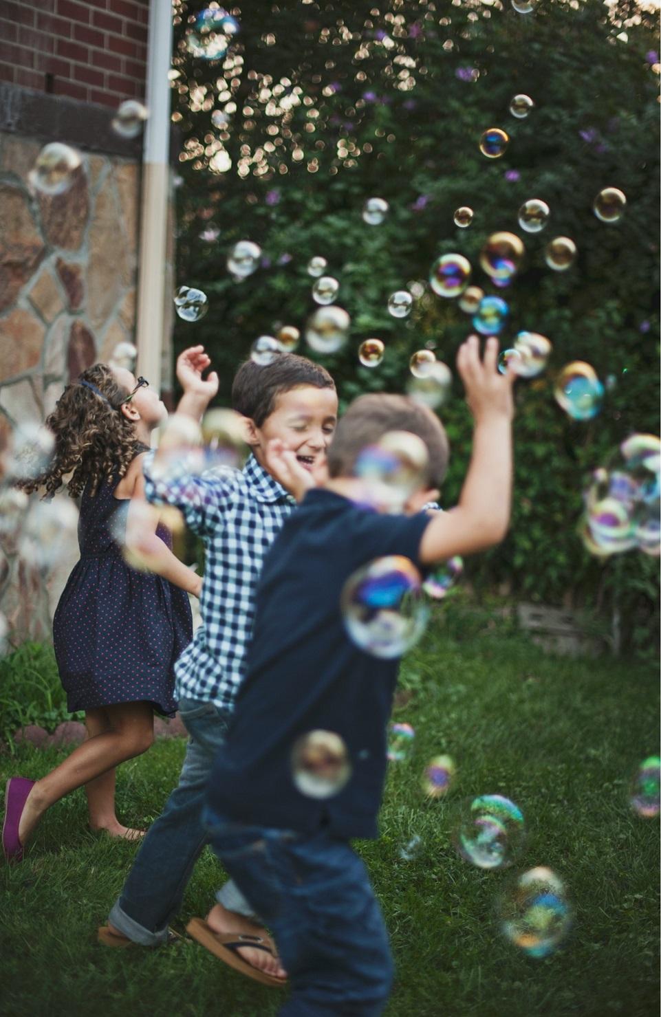 Children dance outside in a cloud of bubbles